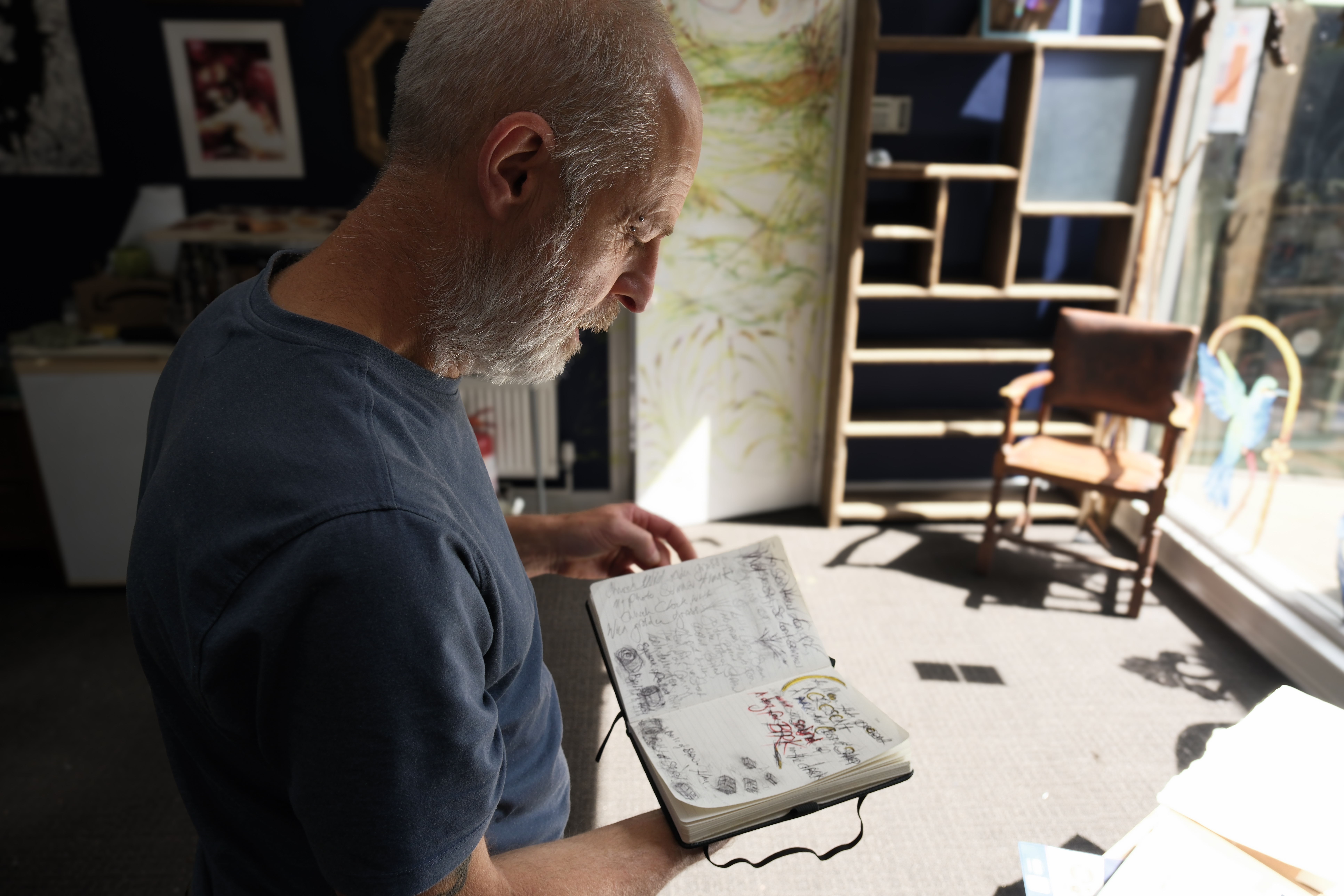 Artist and Service User Paul looking at artist notebook with light streaming in through arts hub window.
