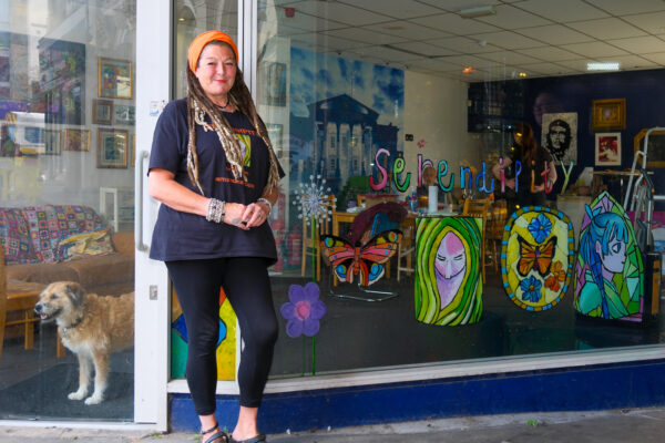 Sonia standing outside the Arts Hub shop window with artwork painted on the shop window.