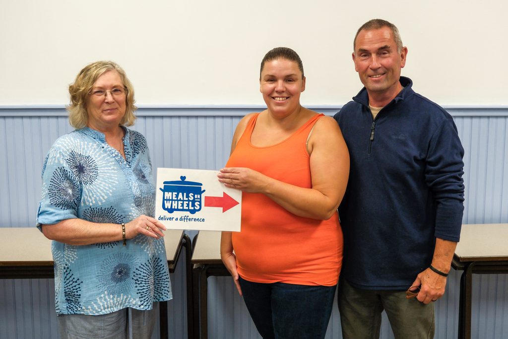 Kim handing Slaithwaite Meals on Wheels sign over to new Volunteer Leads, Sandy and Conrad.